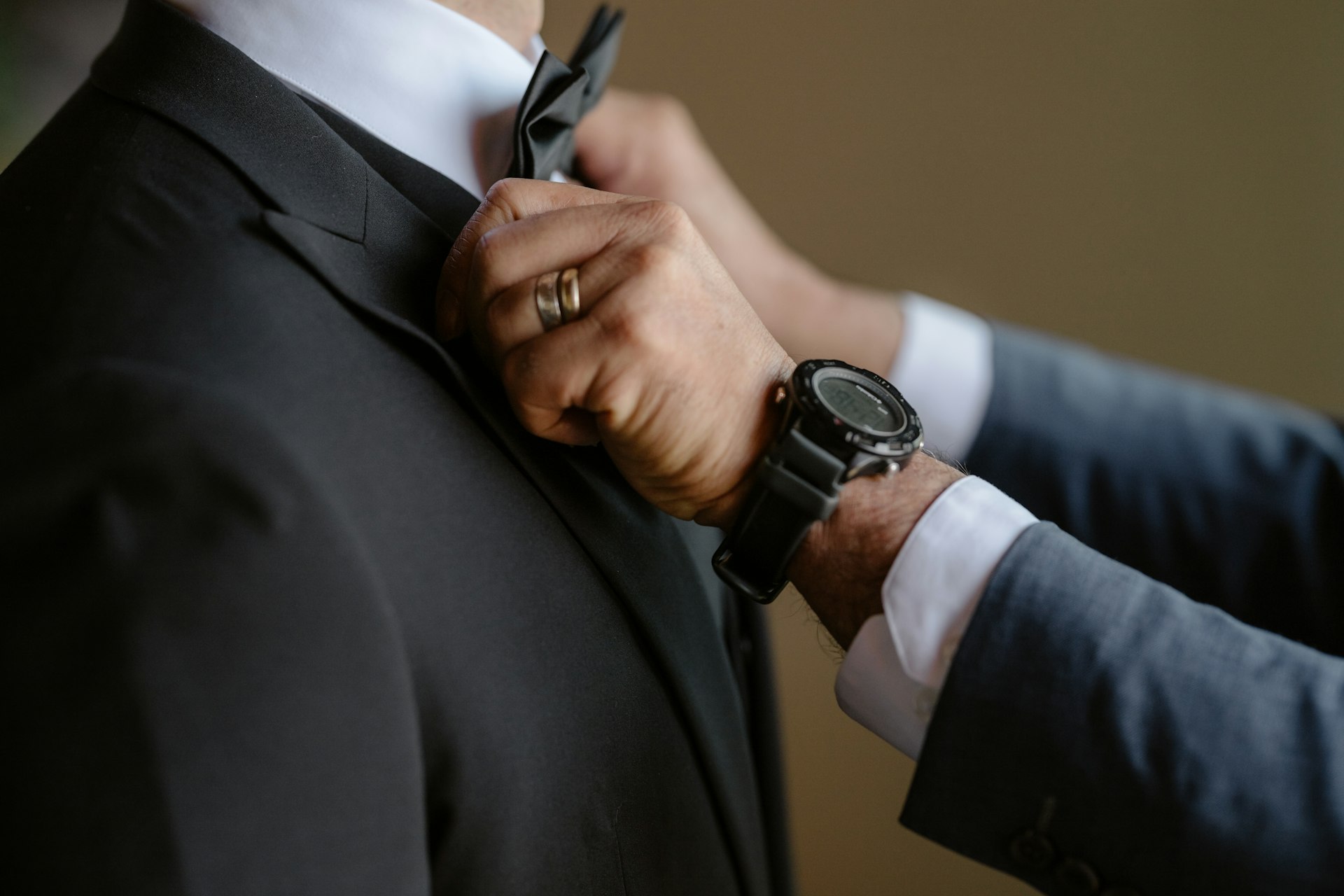 A man adjusts a bow tie on another man.
